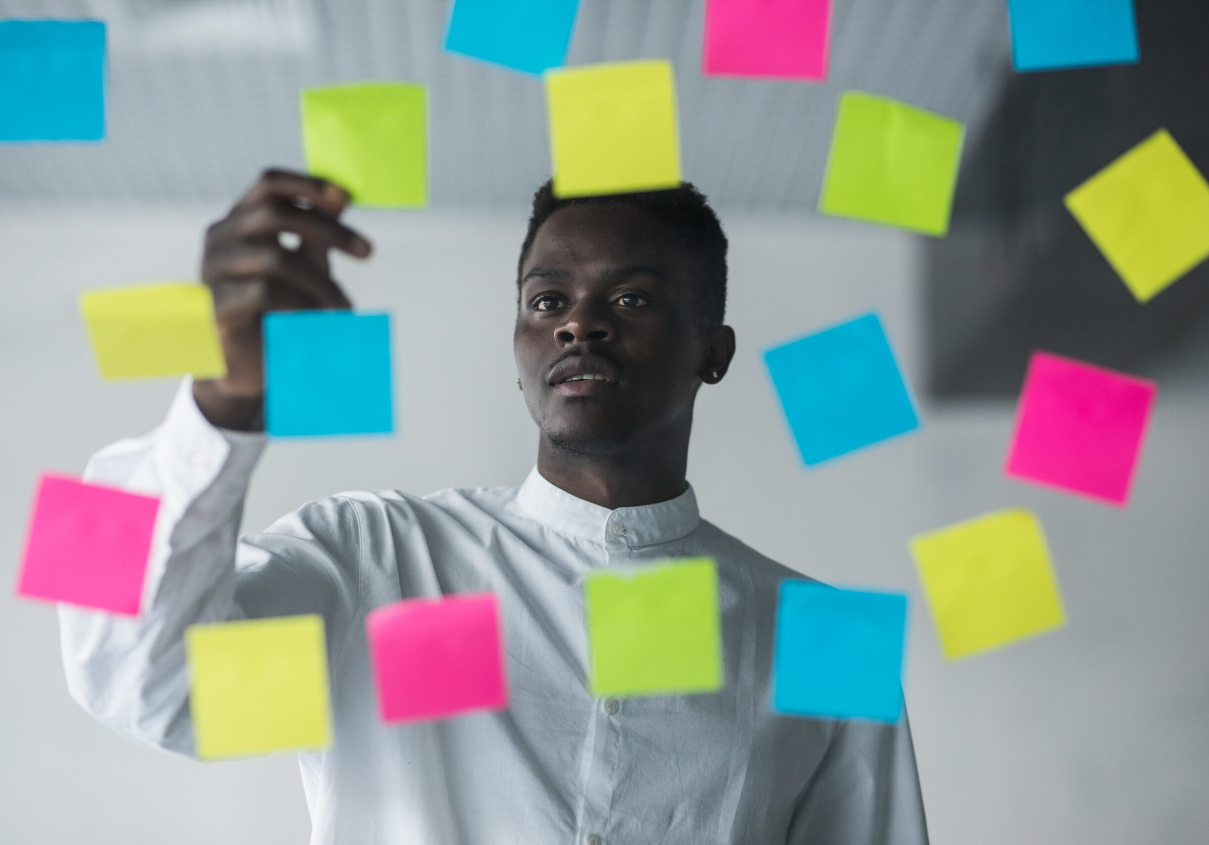 Young afro american business man standing in front of stickers glass wall and write task on sticker at his office place